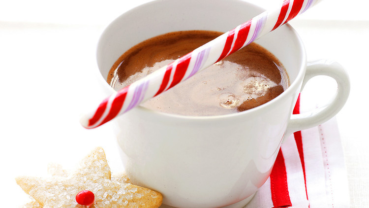 hot cocoa in white mug, candy can balanced across top of mug