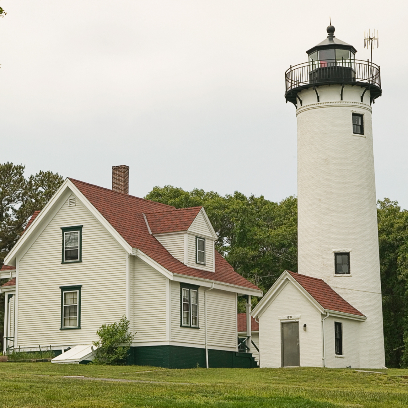 a white light house, next to a white two-story building 