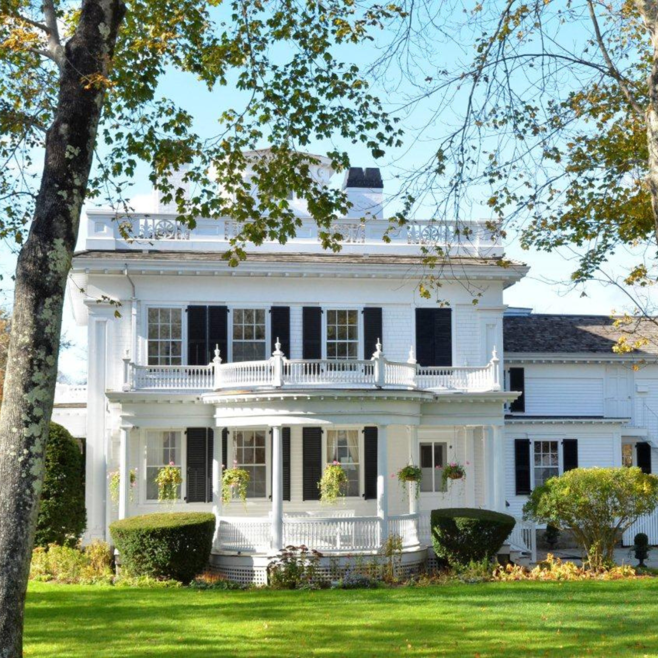 A white, two-story, historic mansion. Black shutters near windows, green lawn.