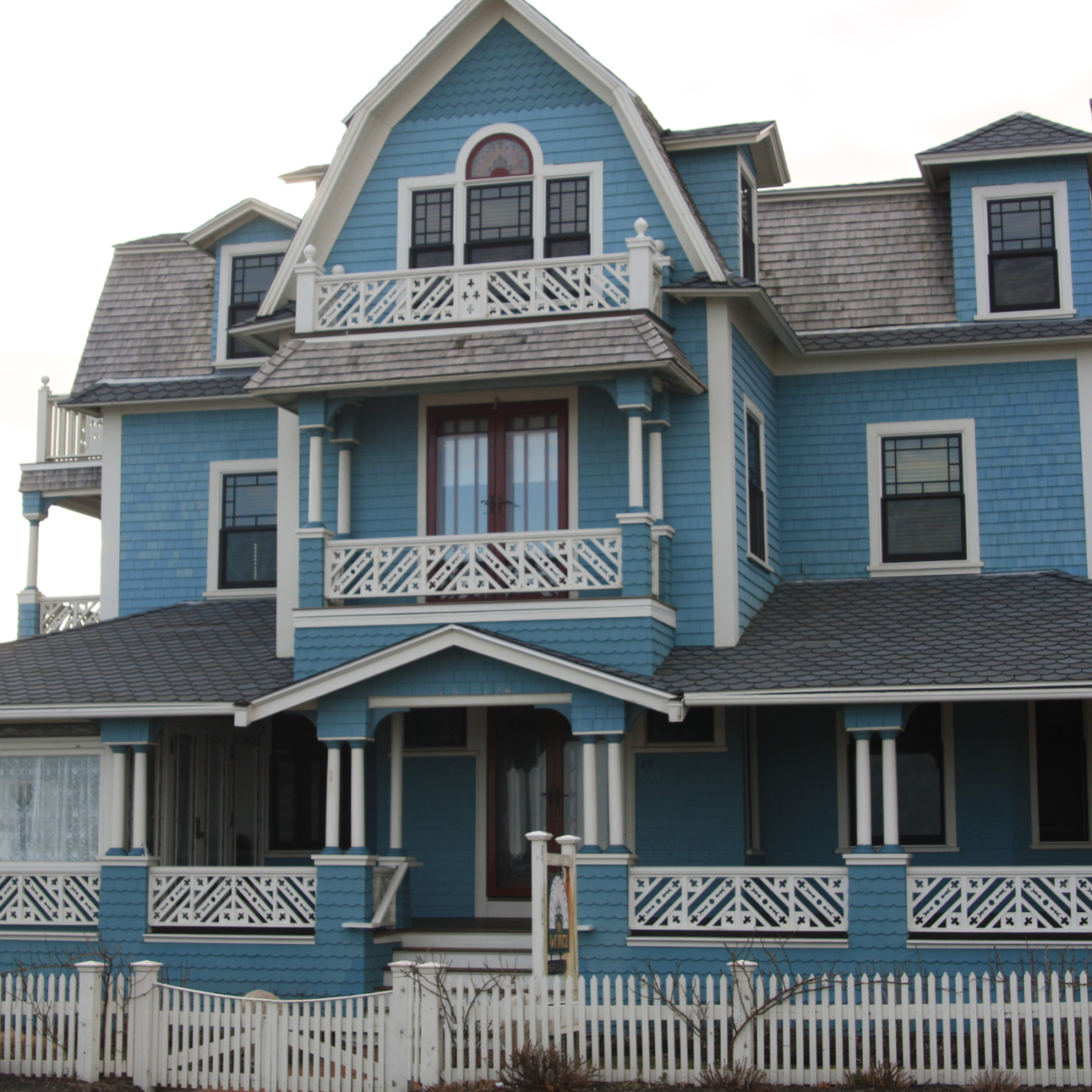 three-story mansion. Light blue, with grey roof. White picket fence.