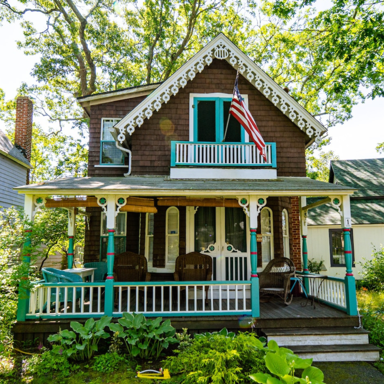A brown gingerbread cottage in Martha's Vineyard.  Trim work on house is a brightly colored teal. An American flag flies in the second floor balcony.