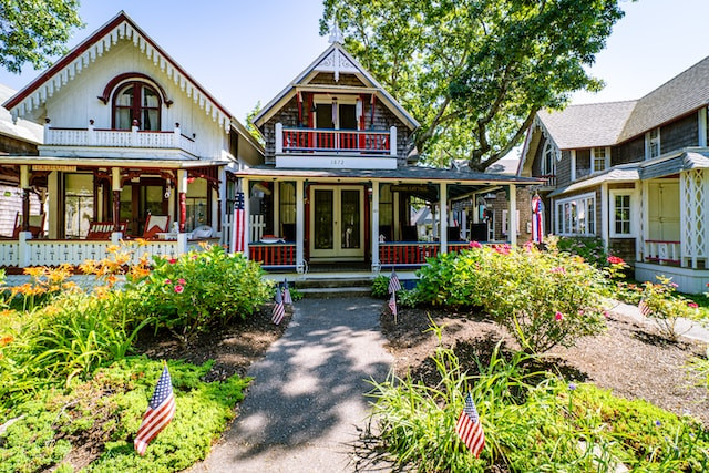 Two quaint, two-story cottages stand. One is white, the other brown. American flags decorate the front yards.