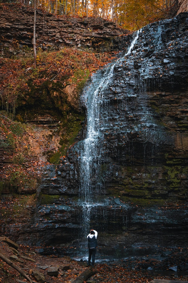 A man looks up, at a very steep waterfall
