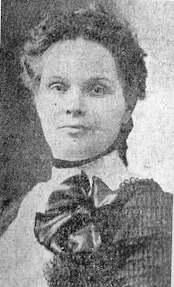 A black and white, historic photograph.  A photo of a woman, looking directly into the camera. Not smiling.